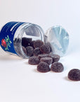 Jar of dark berry gummies spilled on a white surface, representing nighttime wellness and sleep support supplements