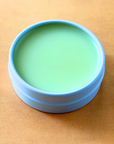 Top view of green CBD balm in a blue jar on a warm-toned surface