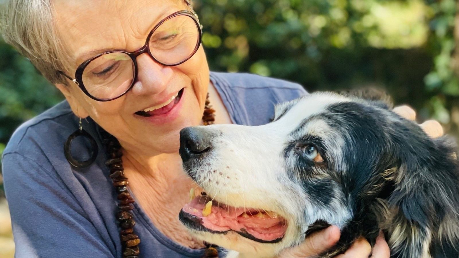 Elderly woman smiling and holding her happy black and white dog outdoors