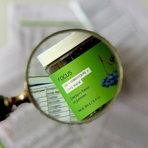 Green label of focus gummies jar magnified by a handheld glass.
