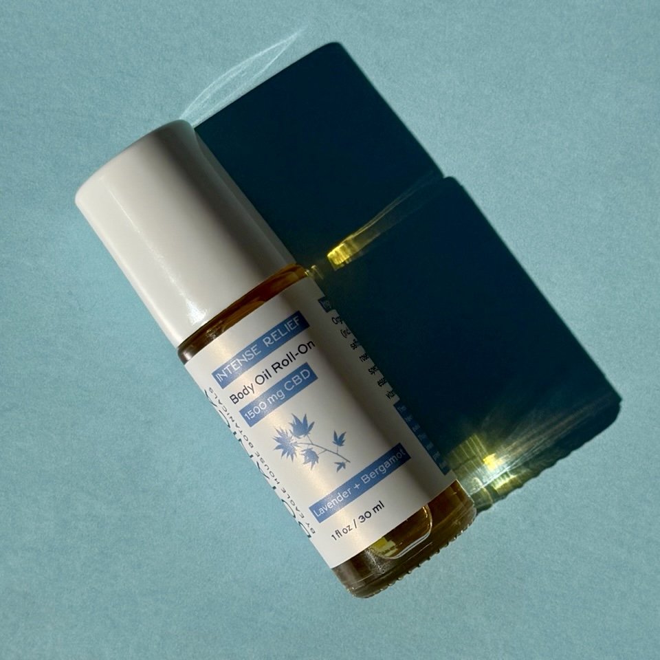 CBD body oil roll-on casting shadow on blue background in direct sunlight.