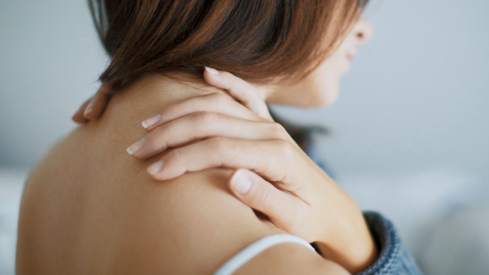 Person gently holding their neck and shoulder, suggesting tension relief, comfort, and muscle relaxation