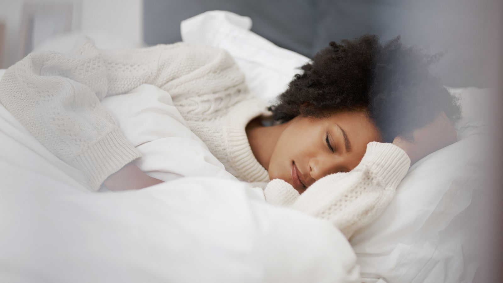 Woman sleeping peacefully in a cozy bed, resting on white pillows and blankets