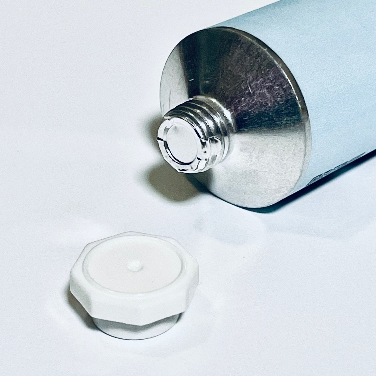 Close-up of sealed aluminum cream tube with white cap removed