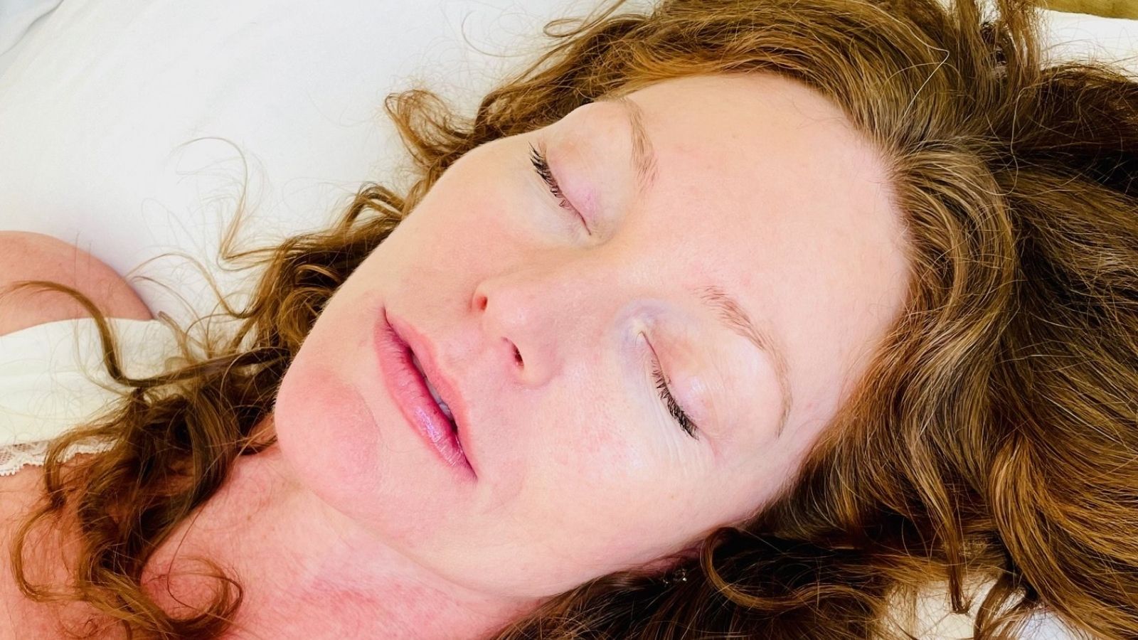 Close-up of a woman resting peacefully with eyes closed, lying on a light surface with soft natural light
