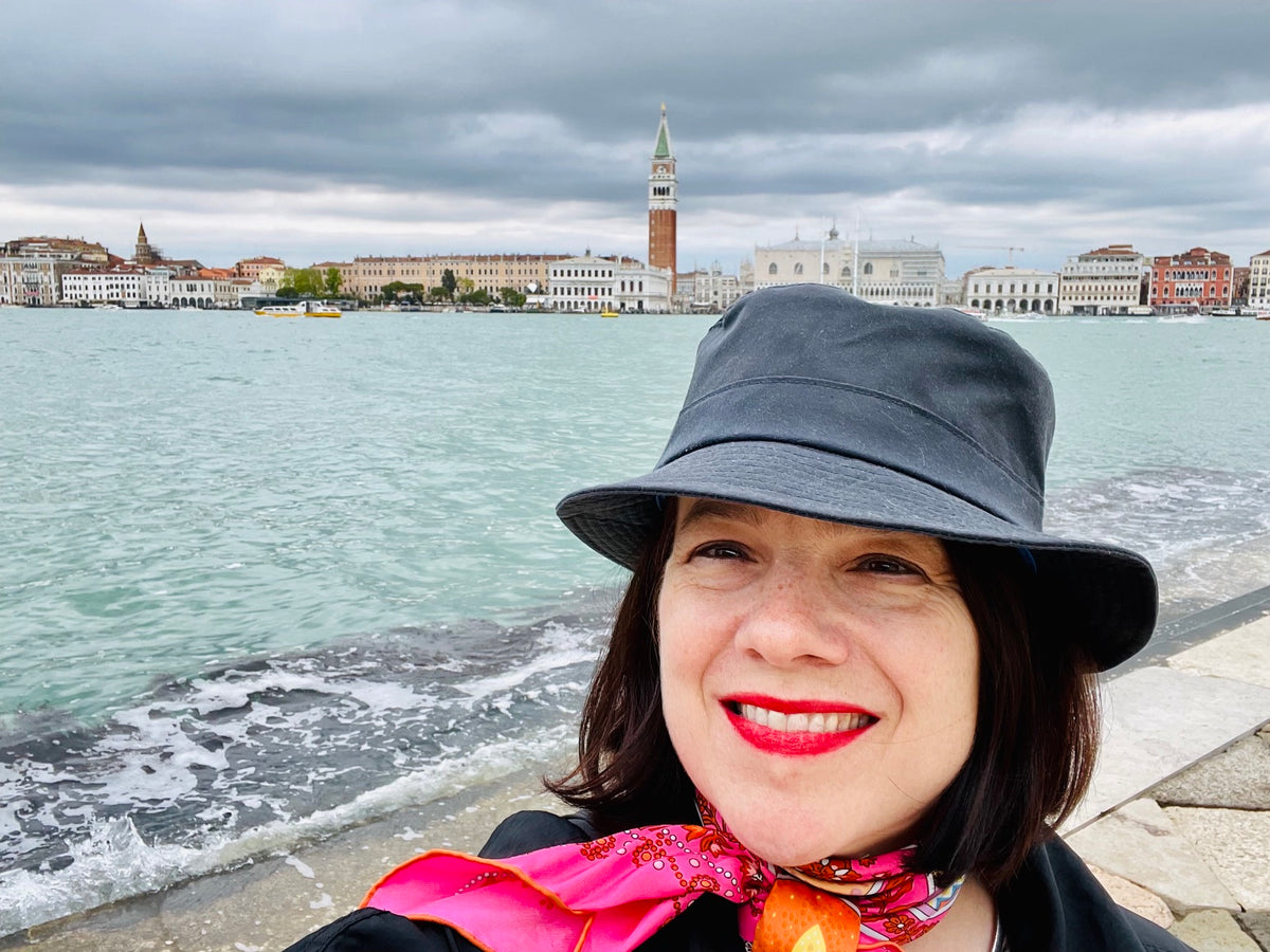 Smiling woman in a black hat by the Venetian Lagoon with the Venice skyline in the background