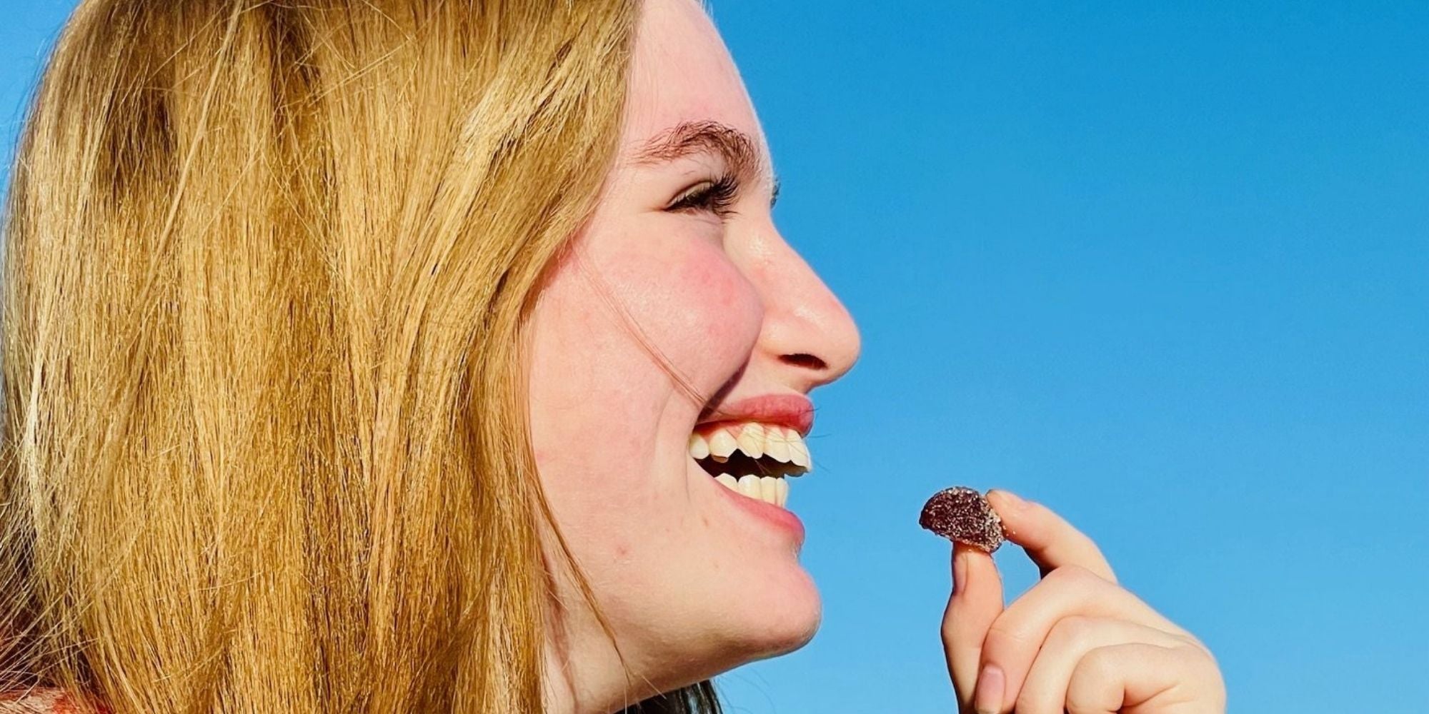 Smiling young woman holding a gummy candy outdoors under a clear blue sky